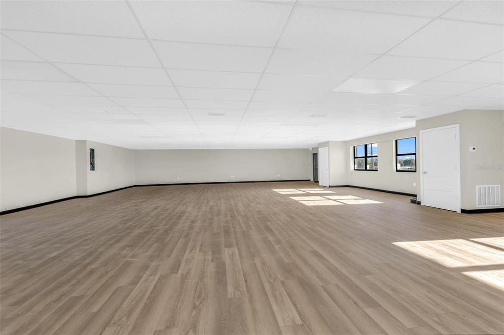 A large, empty room features light wood-look flooring, beige walls, and a white drop ceiling — 3596 TAMIAMI TRAIL, PORT CHARLOTTE, FL