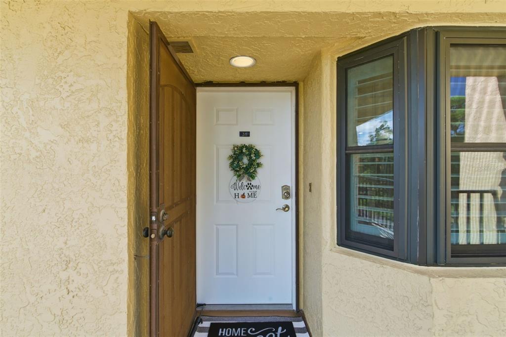 A white front door with a wreath and a screen door stands in a stucco entryway — 5775 PARK STREET N UNIT 311, ST PETERSBURG, FL