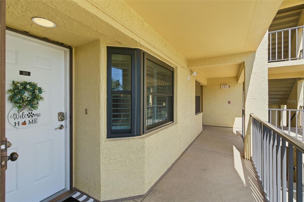 An exterior view of a yellow apartment building hallway with a white front door — 5775 PARK STREET N UNIT 311, ST PETERSBURG, FL