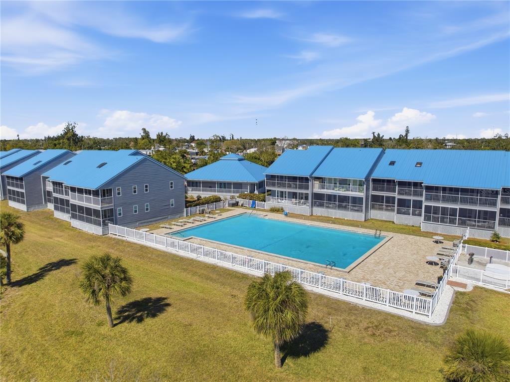 An aerial view shows a swimming pool situated between two multi-story residential buildings with blue roofs — 4410 WARREN AVENUE UNIT 108, PORT CHARLOTTE, FL