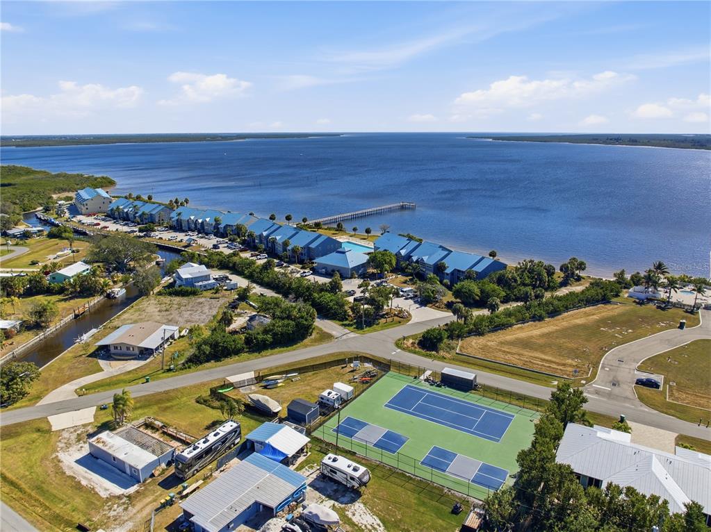 An aerial view shows a waterfront residential complex with a tennis court in the foreground — 4410 WARREN AVENUE UNIT 108, PORT CHARLOTTE, FL