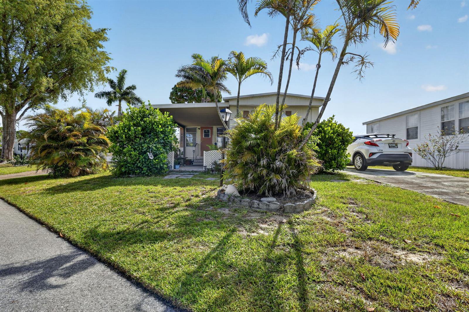 A single-story mobile home with a front porch, palm trees, and a parked white car — 12375 S Military Trail # 90, Boynton Beach FL 33436, BOYNTON BEACH, FL