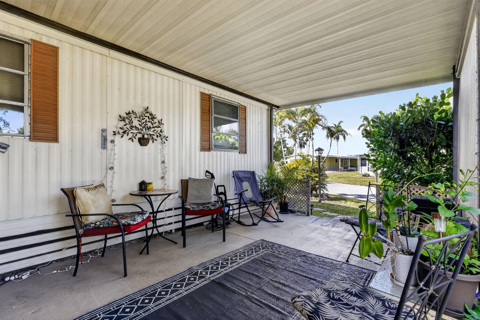 A covered concrete patio features outdoor furniture, a patterned rug, and potted plants — 12375 S Military Trail # 90, Boynton Beach FL 33436, BOYNTON BEACH, FL