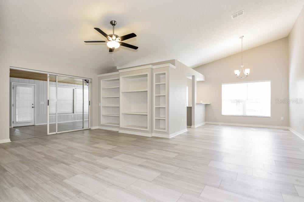 A bright living room features light wood-look flooring, a ceiling fan, and built-in shelving — 26808 HAVERHILL DRIVE, LUTZ, FL