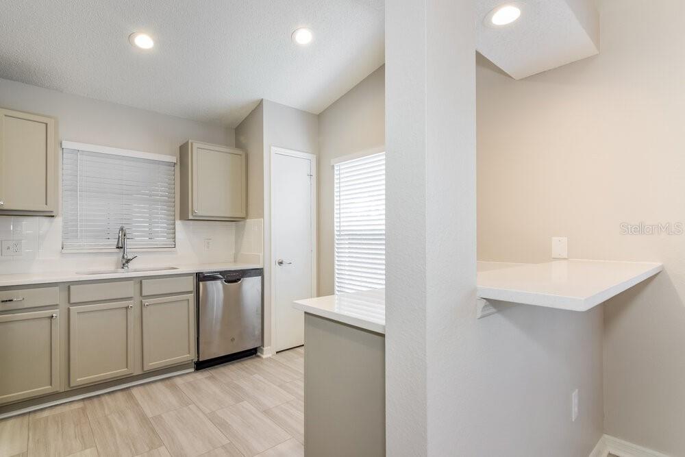 A kitchen features light gray cabinets, white countertops, stainless steel appliances, and wood-look flooring — 26808 HAVERHILL DRIVE, LUTZ, FL