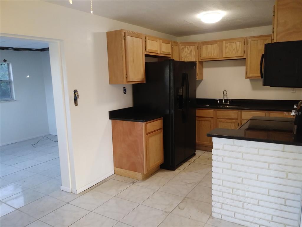 A kitchen features light wood cabinets, black countertops, a black refrigerator, and white tile flooring — 2183 PATTERSON AVENUE, ORLANDO, FL