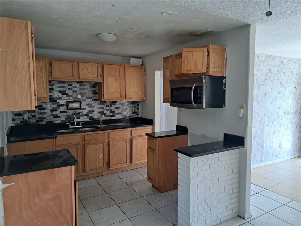 A kitchen features oak cabinets, black countertops, a tiled backsplash, and a white brick peninsula — 2183 PATTERSON AVENUE, ORLANDO, FL