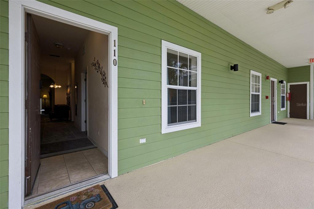 An open doorway leads into a home with green siding and a covered concrete walkway — 110 WATLING WAY, DAVENPORT, FL
