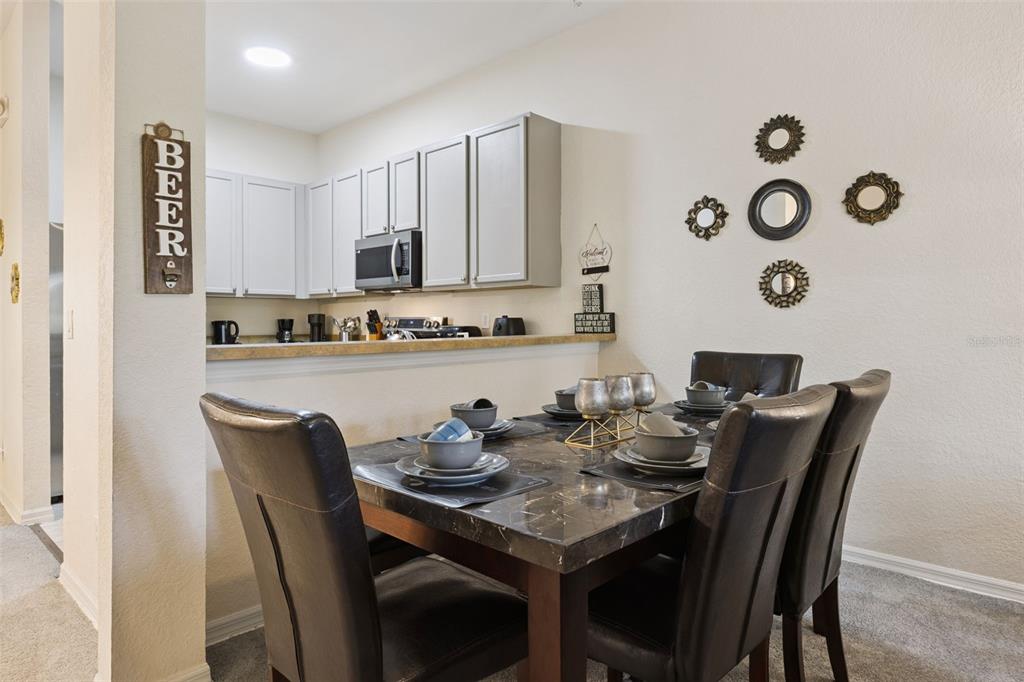 A dining area with a marble-topped table sits adjacent to a kitchen with white cabinets — 110 WATLING WAY, DAVENPORT, FL