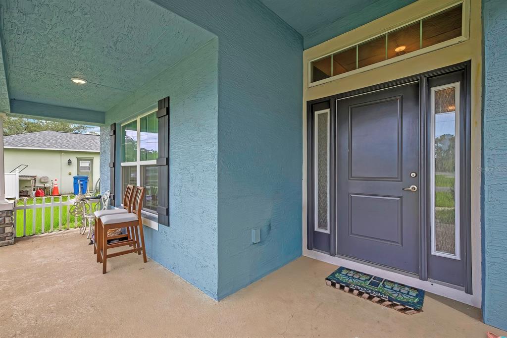 A covered front porch with blue stucco walls, a dark gray door, and two chairs — 10358 MUSA ROAD, SPRING HILL, FL