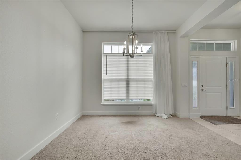A carpeted dining room features a chandelier, a large window with blinds, and white walls — 10358 MUSA ROAD, SPRING HILL, FL