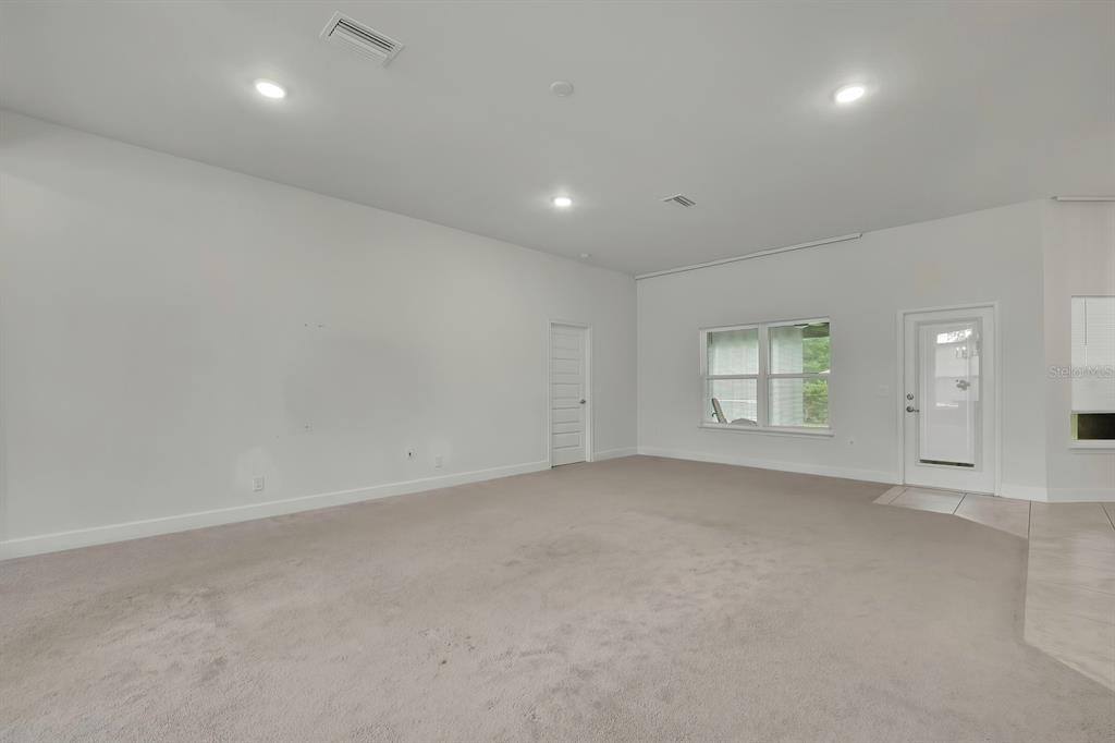An empty living room with beige carpeting, white walls, recessed lighting, and a glass door — 10358 MUSA ROAD, SPRING HILL, FL
