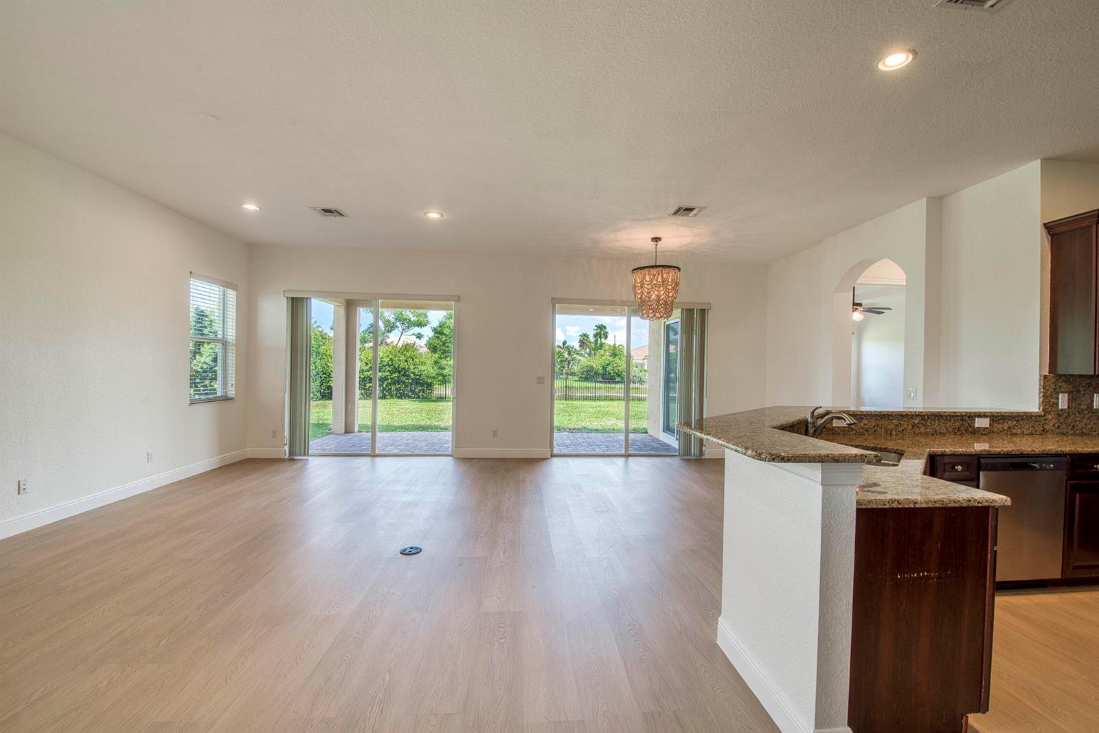 An open-concept living area features light wood flooring, a kitchen island, and sliding glass doors — 172 Manor Circle, Jupiter FL 33458, JUPITER, FL