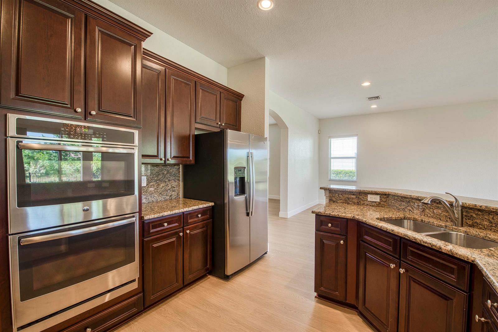 A kitchen features dark wood cabinets, granite countertops, stainless steel appliances, and light wood flooring — 172 Manor Circle, Jupiter FL 33458, JUPITER, FL