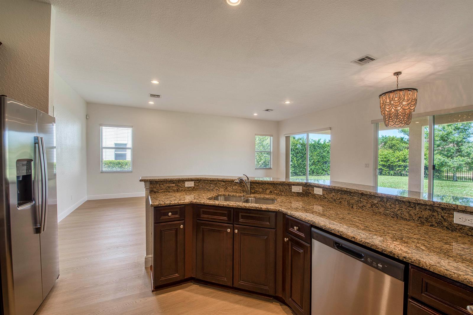 A kitchen with dark wood cabinets, granite countertops, stainless steel appliances, and light wood flooring — 172 Manor Circle, Jupiter FL 33458, JUPITER, FL