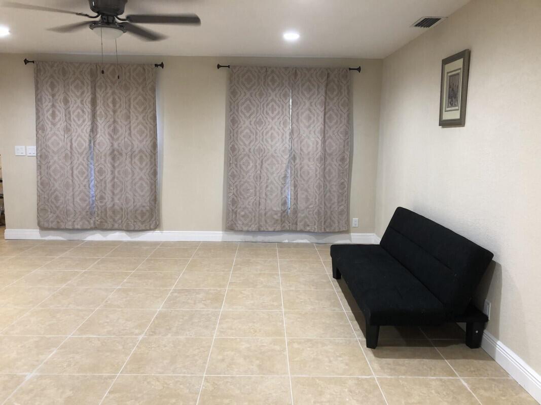 A living room features beige tile flooring, two curtained windows, and a black futon sofa — 279 SE 8th Terrace # A, Deerfield Beach FL 33441, DEERFIELD BEACH, FL