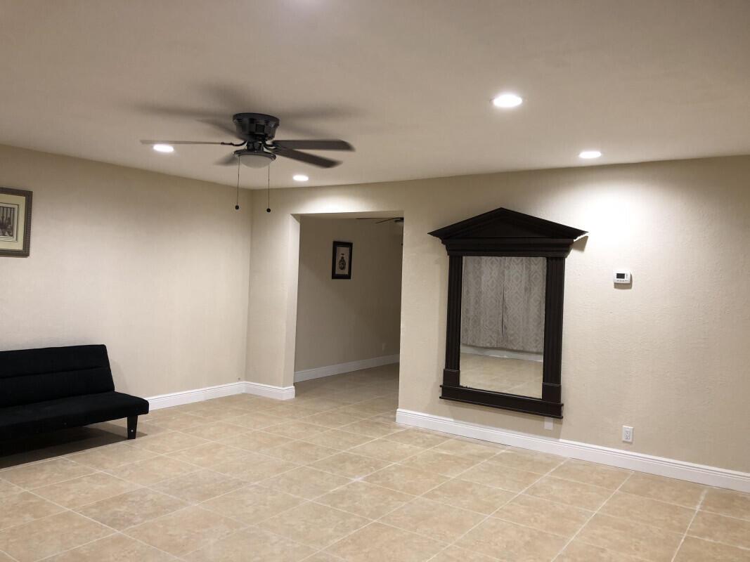 A living room with beige tile floors, a black futon, a ceiling fan, and a mirror — 279 SE 8th Terrace # A, Deerfield Beach FL 33441, DEERFIELD BEACH, FL