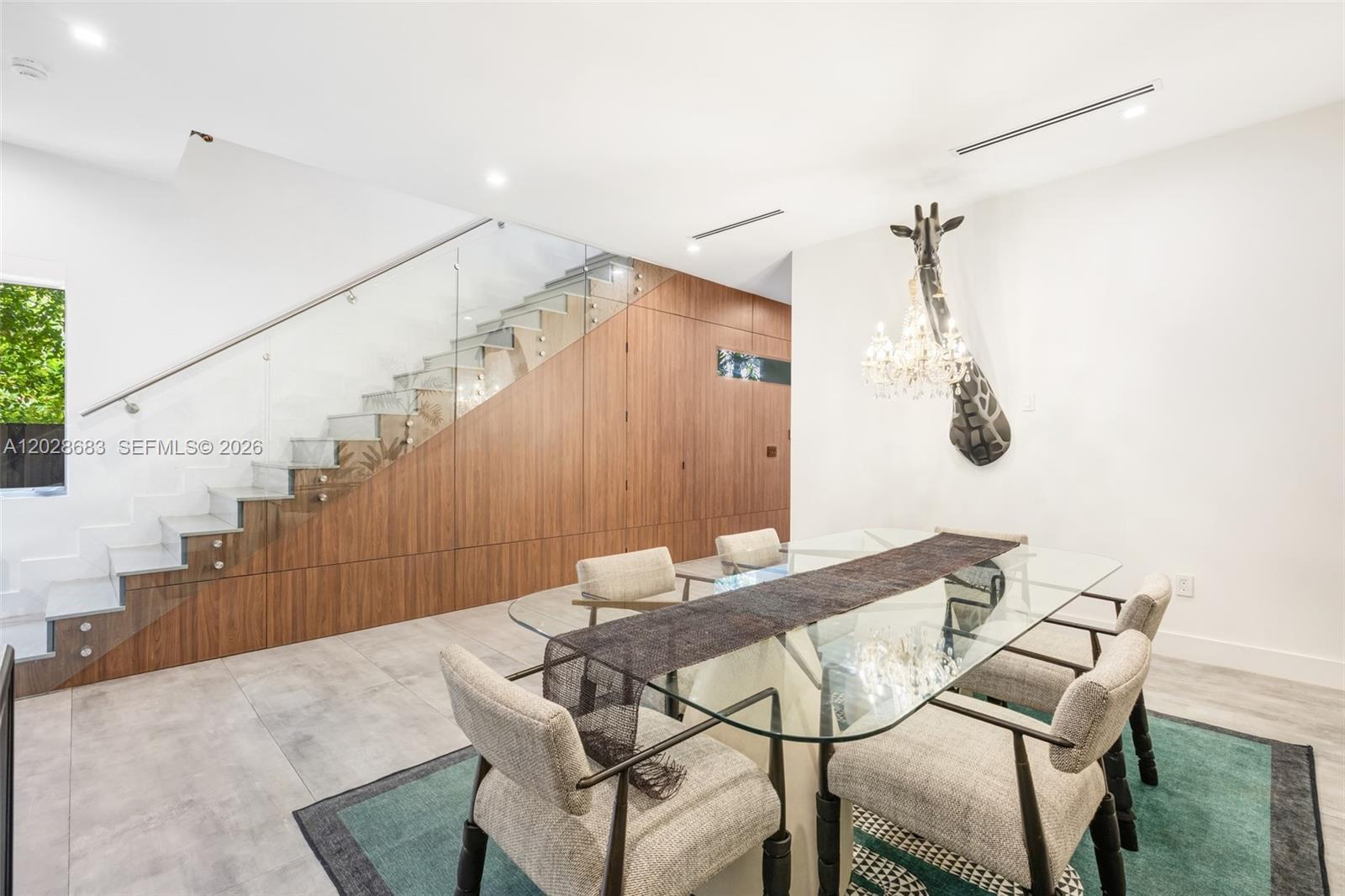 A dining room features a glass table, a giraffe-themed chandelier, and a wood-paneled staircase — 3135 Ohio St # 3135, Miami FL 33133, MIAMI, FL