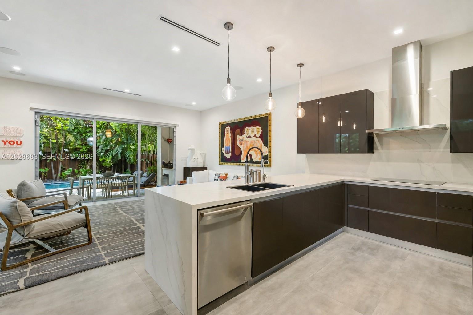 A modern kitchen features dark cabinetry, a white stone island, and sliding doors to a patio — 3135 Ohio St # 3135, Miami FL 33133, MIAMI, FL