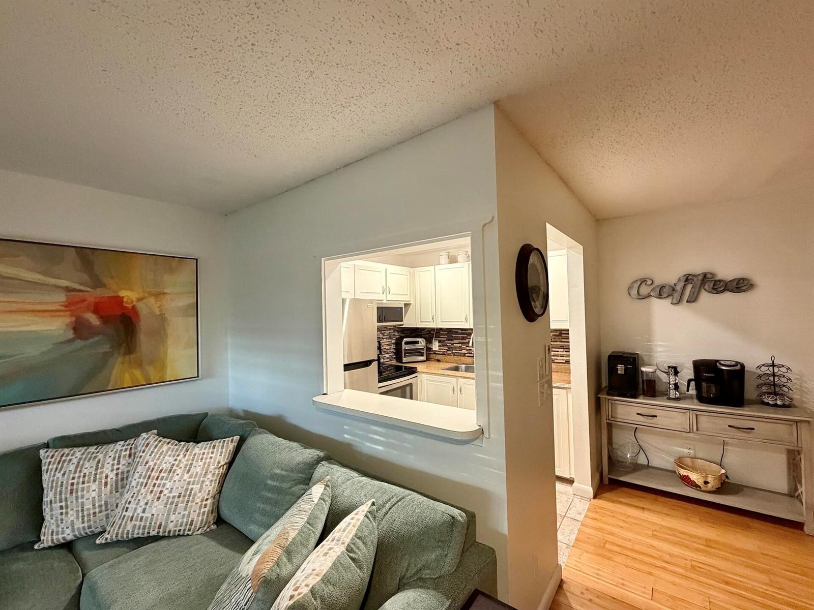 A living room with a green sofa overlooks a kitchen through a pass-through window — 335 Durham Circle # J, Deerfield Beach FL 33442, DEERFIELD BEACH, FL