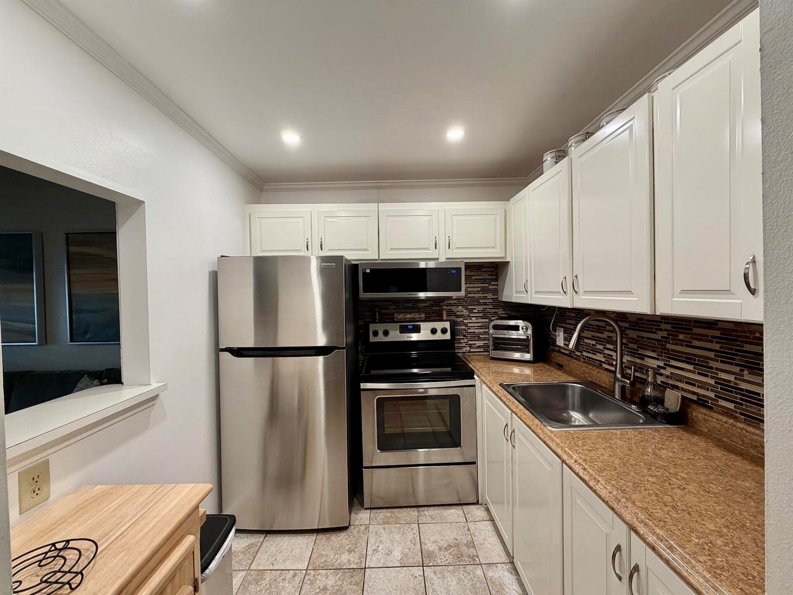 A kitchen features white cabinets, stainless steel appliances, a brown countertop, and a tiled backsplash — 335 Durham Circle # J, Deerfield Beach FL 33442, DEERFIELD BEACH, FL