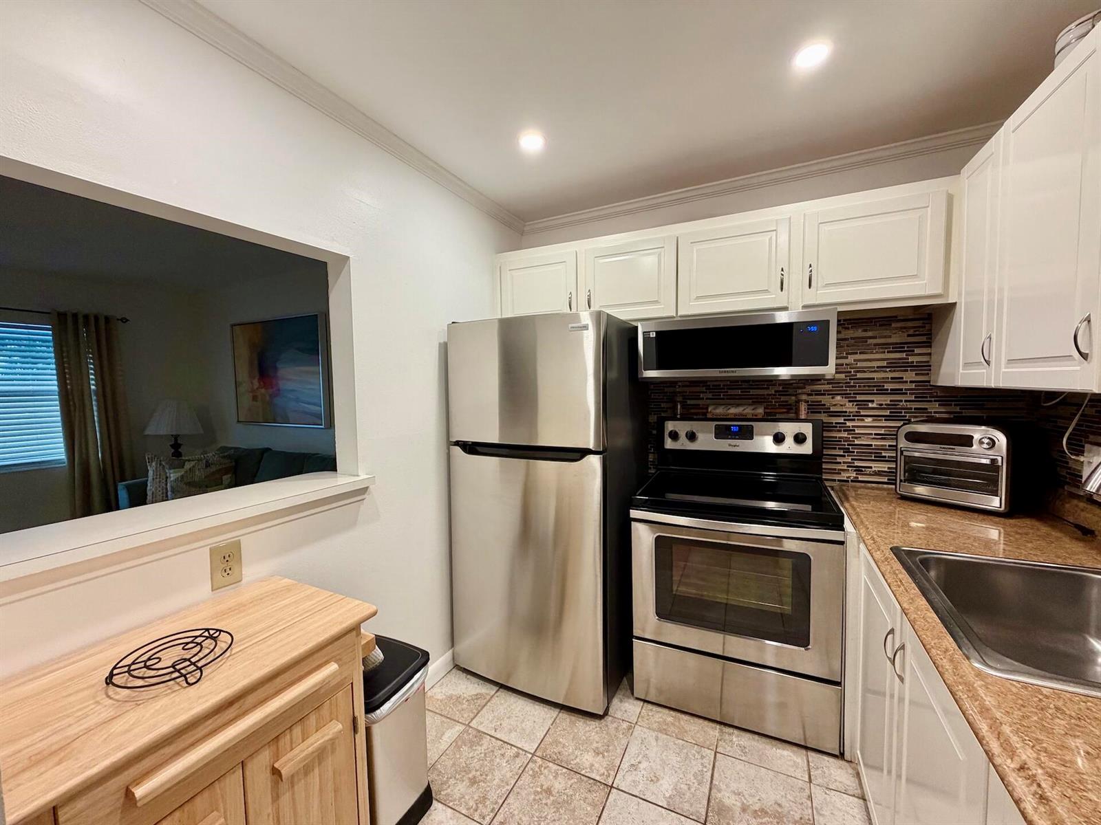 A kitchen features stainless steel appliances, white cabinets, and a pass-through window to the living area — 335 Durham Circle # J, Deerfield Beach FL 33442, DEERFIELD BEACH, FL