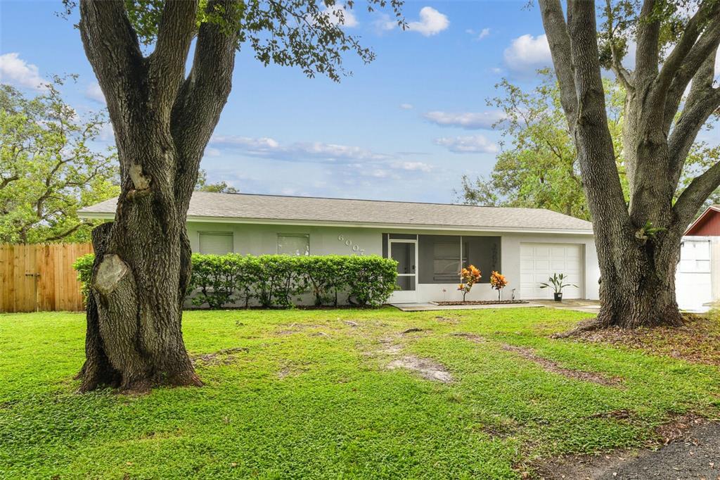 A single-story house with a white garage, a screened entryway, and large trees in front — 6007 CALENDAR COURT W, LAKELAND, FL