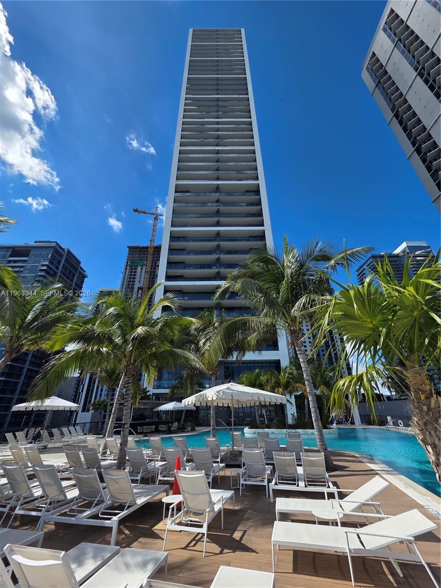 A tall residential skyscraper rises above a pool deck furnished with lounge chairs and umbrellas — 159 NE 6th street # 3311, Miami FL 33132, MIAMI, FL