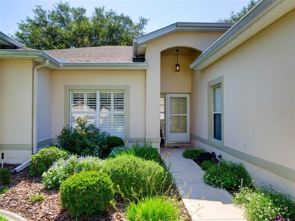 A beige house exterior features a covered entryway, a concrete walkway, and landscaped garden beds — 3701 PLANTATION BOULEVARD, LEESBURG, FL