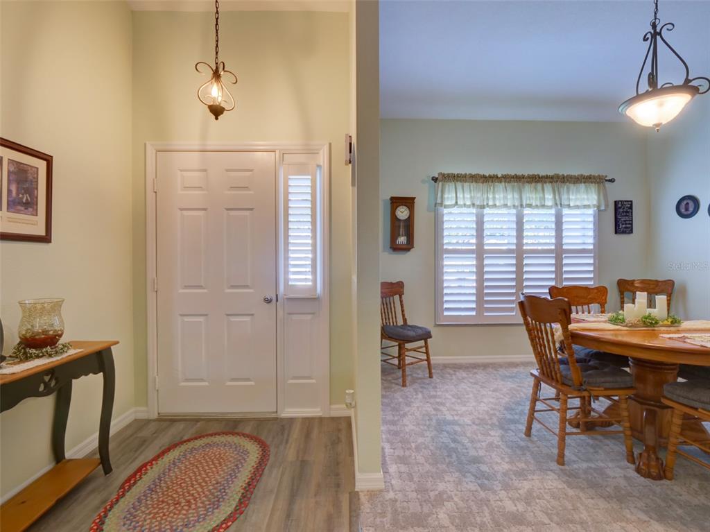 An entryway with wood-look flooring leads into a dining room featuring carpet and plantation shutters — 3701 PLANTATION BOULEVARD, LEESBURG, FL