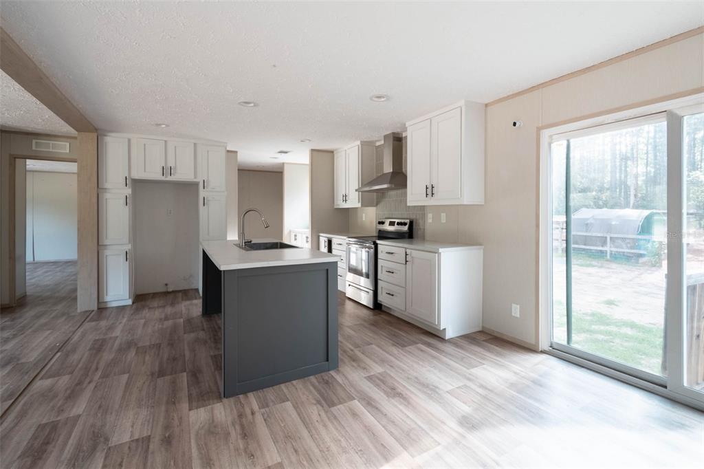 A kitchen with white cabinets, a dark gray island, stainless steel appliances, and sliding doors — 8719 N PRESNELL TERRACE, DUNNELLON, FL