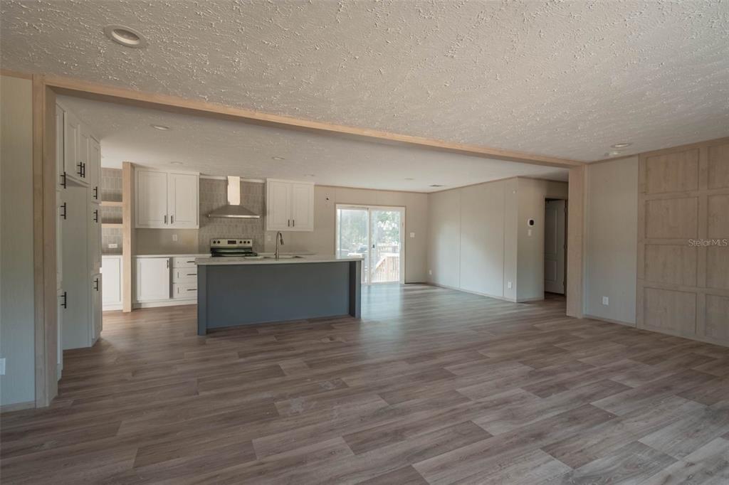 An open-concept kitchen and living area featuring white cabinets, a gray island, and wood-look flooring — 8719 N PRESNELL TERRACE, DUNNELLON, FL