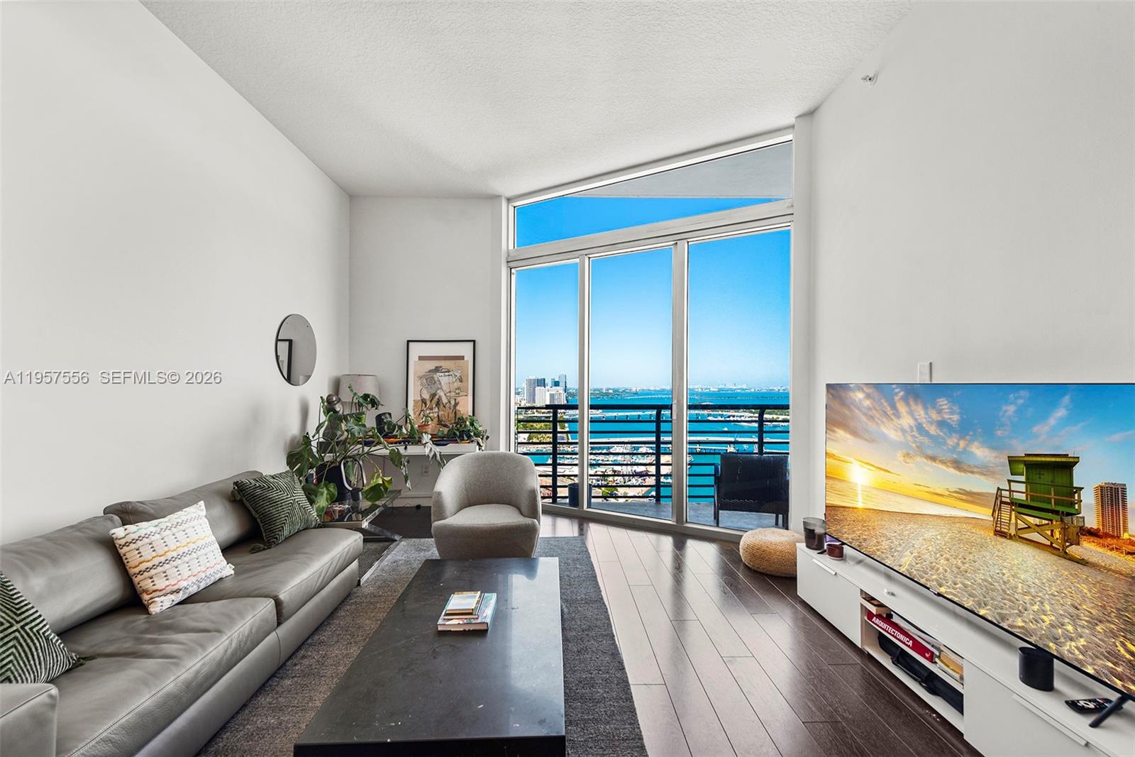 A living room features a grey leather sofa, dark wood floors, and floor-to-ceiling windows — 335 S Biscayne Blvd # 10, Miami FL 33131, MIAMI, FL