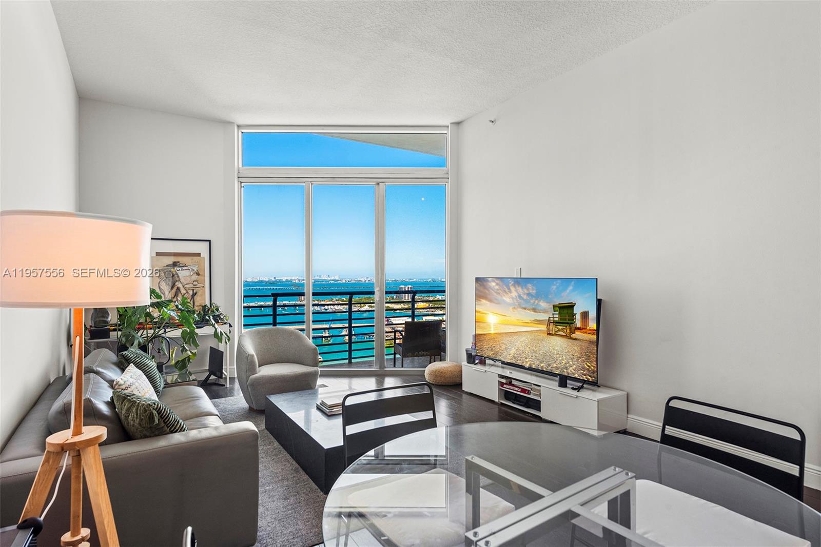 A living room features a grey sofa, a glass dining table, and floor-to-ceiling balcony windows — 335 S Biscayne Blvd # 10, Miami FL 33131, MIAMI, FL