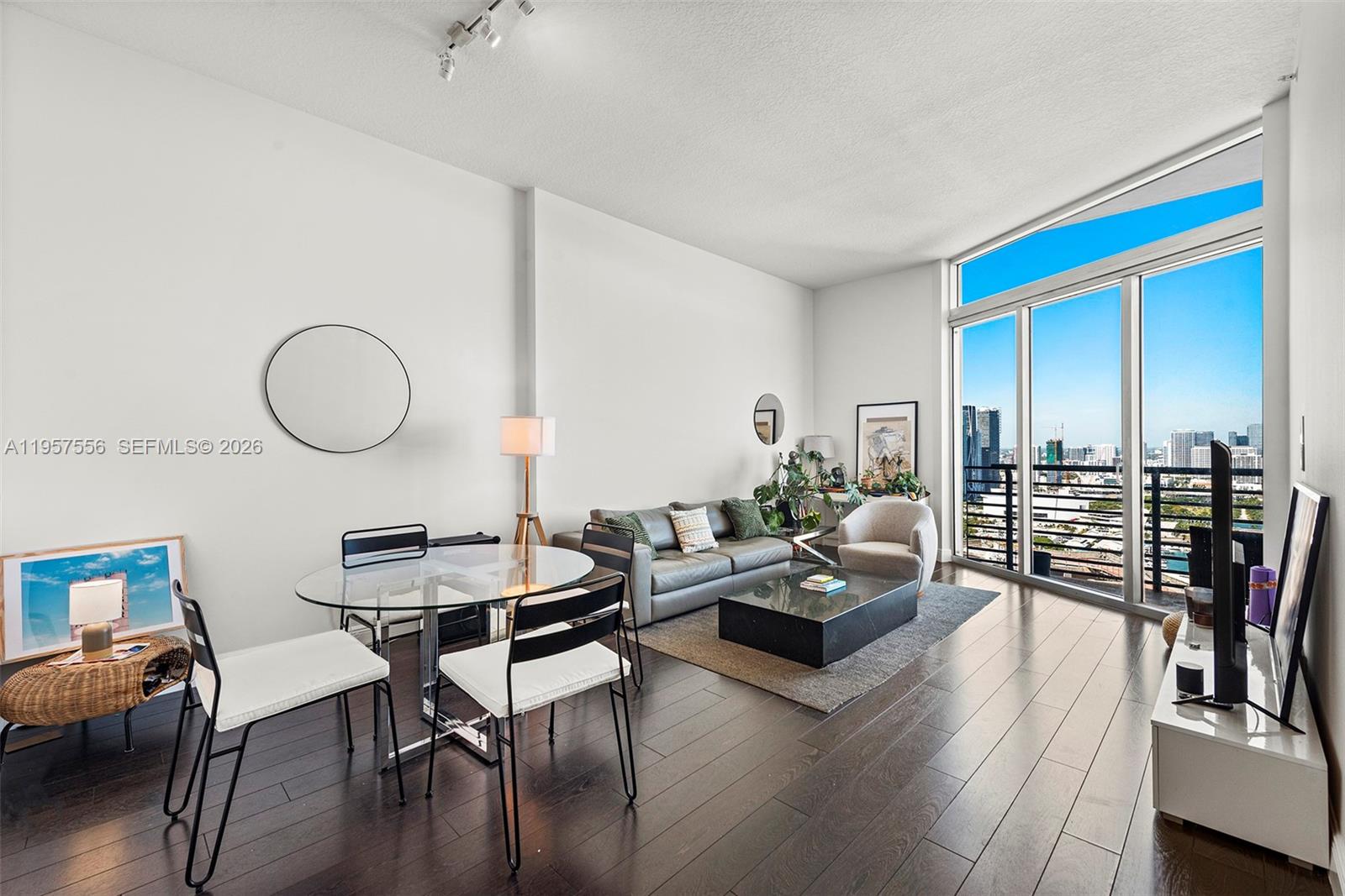 A modern living and dining area features dark hardwood floors, floor-to-ceiling windows, and city views — 335 S Biscayne Blvd # 10, Miami FL 33131, MIAMI, FL