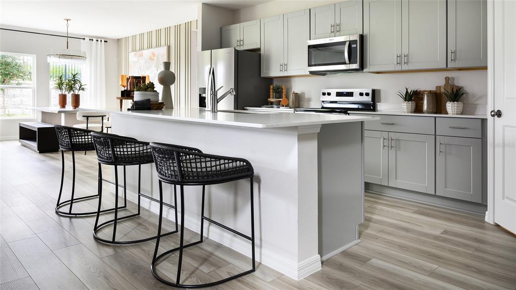 A modern kitchen features gray cabinets, a white island with black stools, and wood-look flooring — 36656 THORNHEDGE DRIVE, ZEPHYRHILLS, FL