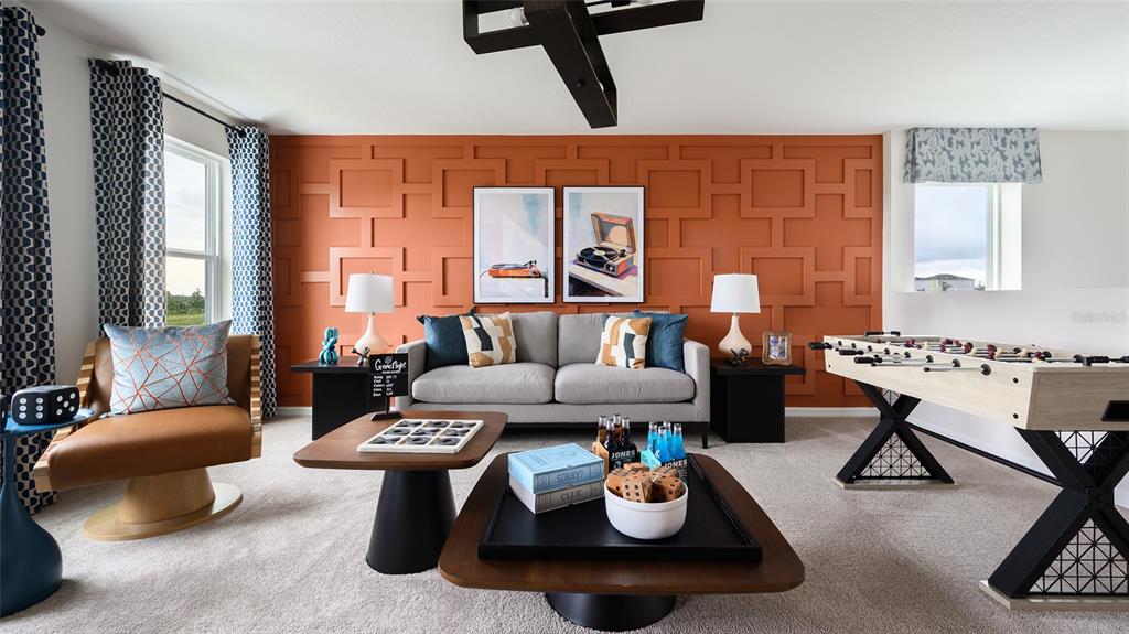 A game room features a grey sofa, foosball table, and a geometric orange accent wall — 36656 THORNHEDGE DRIVE, ZEPHYRHILLS, FL