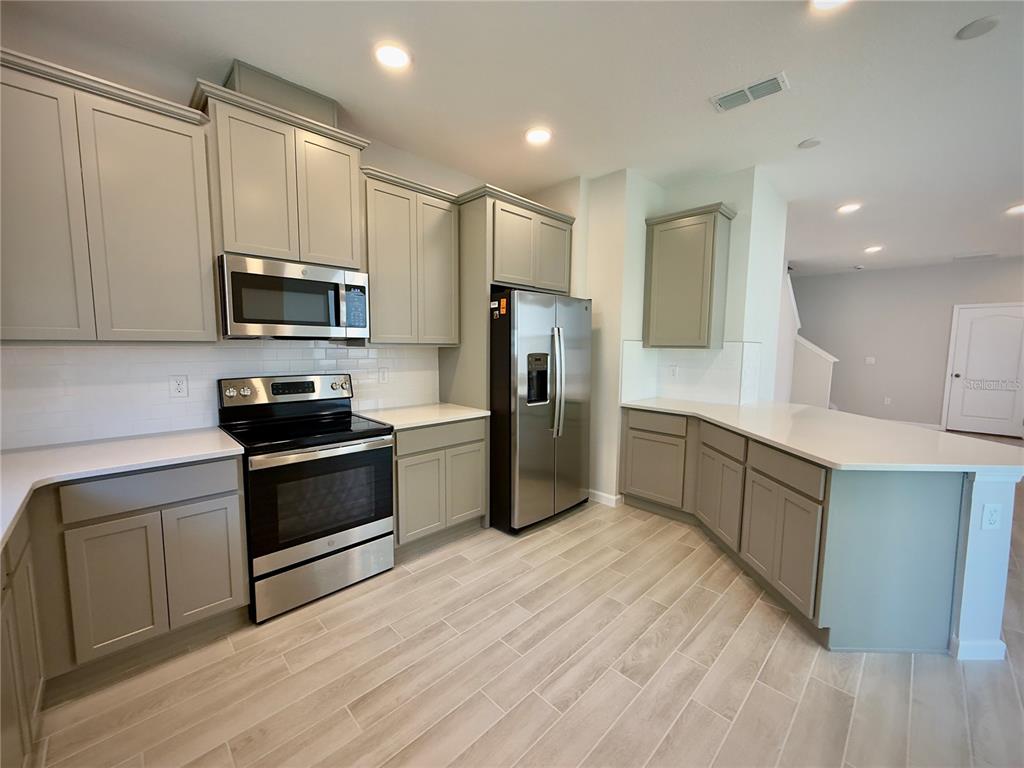 A kitchen features light gray cabinets, stainless steel appliances, white countertops, and wood-look tile flooring — 4762 STERNWHEELER LANE, OVIEDO, FL