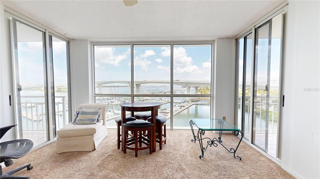 A sunroom features floor-to-ceiling windows overlooking a marina and bridge with carpeted flooring — 100 PIERCE STREET UNIT 601, CLEARWATER, FL