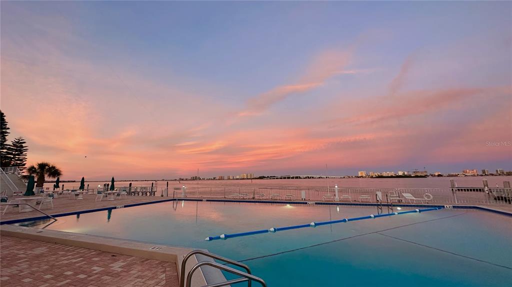 A swimming pool overlooks a bay at sunset with a distant city skyline — 100 PIERCE STREET UNIT 601, CLEARWATER, FL