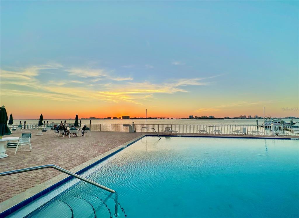 A swimming pool overlooks a bay with a sunset view and a distant city skyline — 100 PIERCE STREET UNIT 601, CLEARWATER, FL