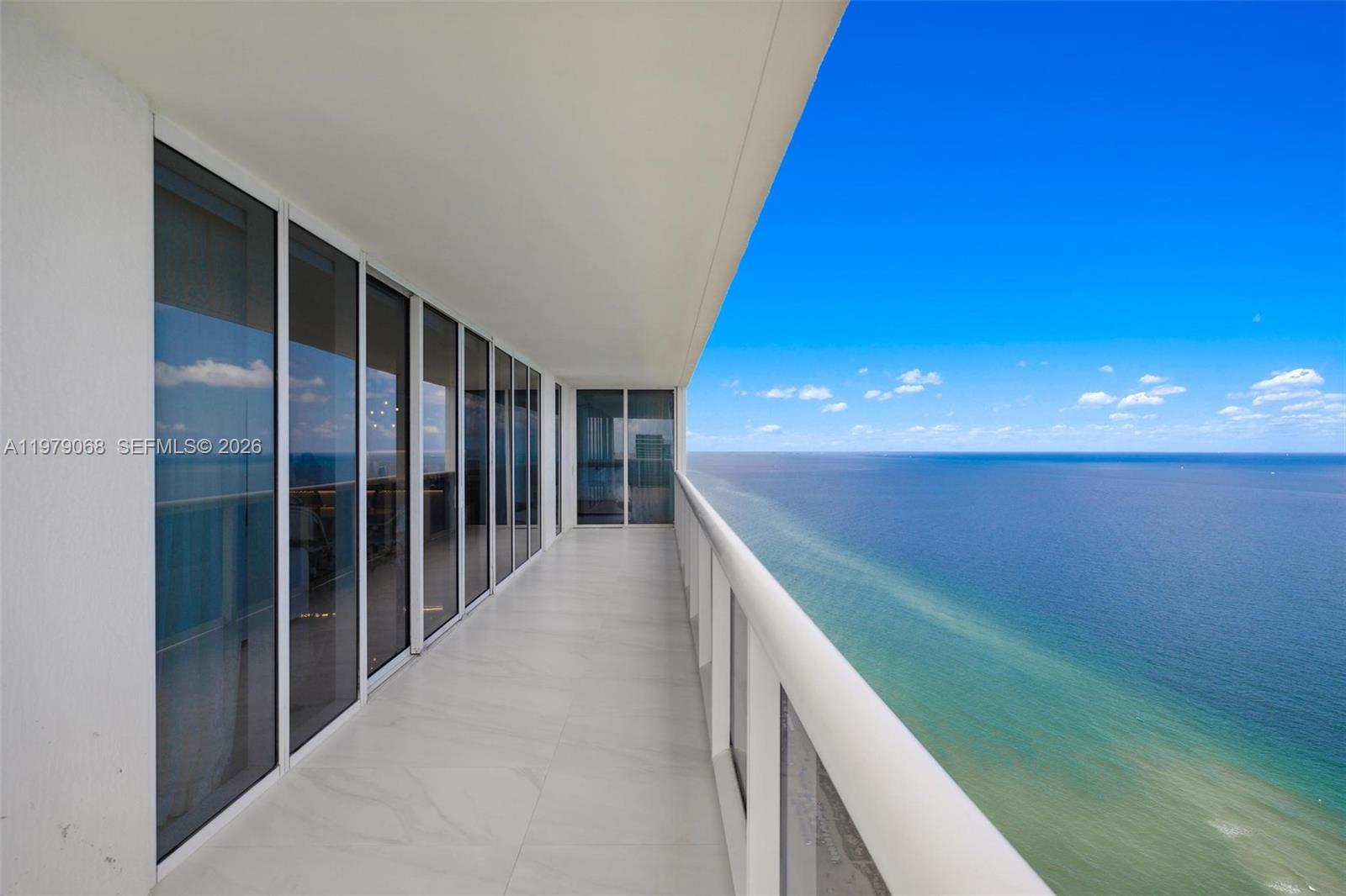 A long, tiled balcony features glass railings overlooking the ocean under a clear blue sky — 1830 S Ocean Dr # 4502, Hallandale Beach FL 33009, HALLANDALE BEACH, FL