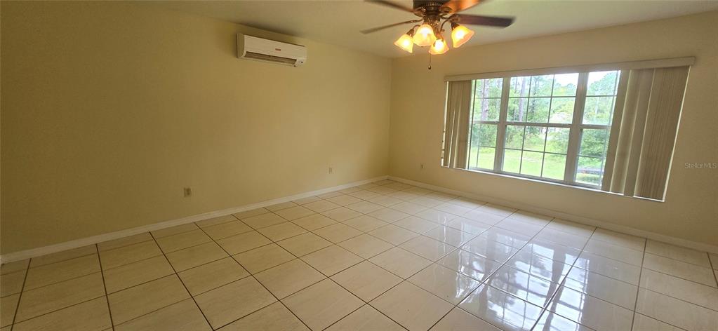 An empty room features light-colored tile flooring, a ceiling fan, and a wall-mounted air conditioner — 15209 SW 46 CIRCLE, OCALA, FL