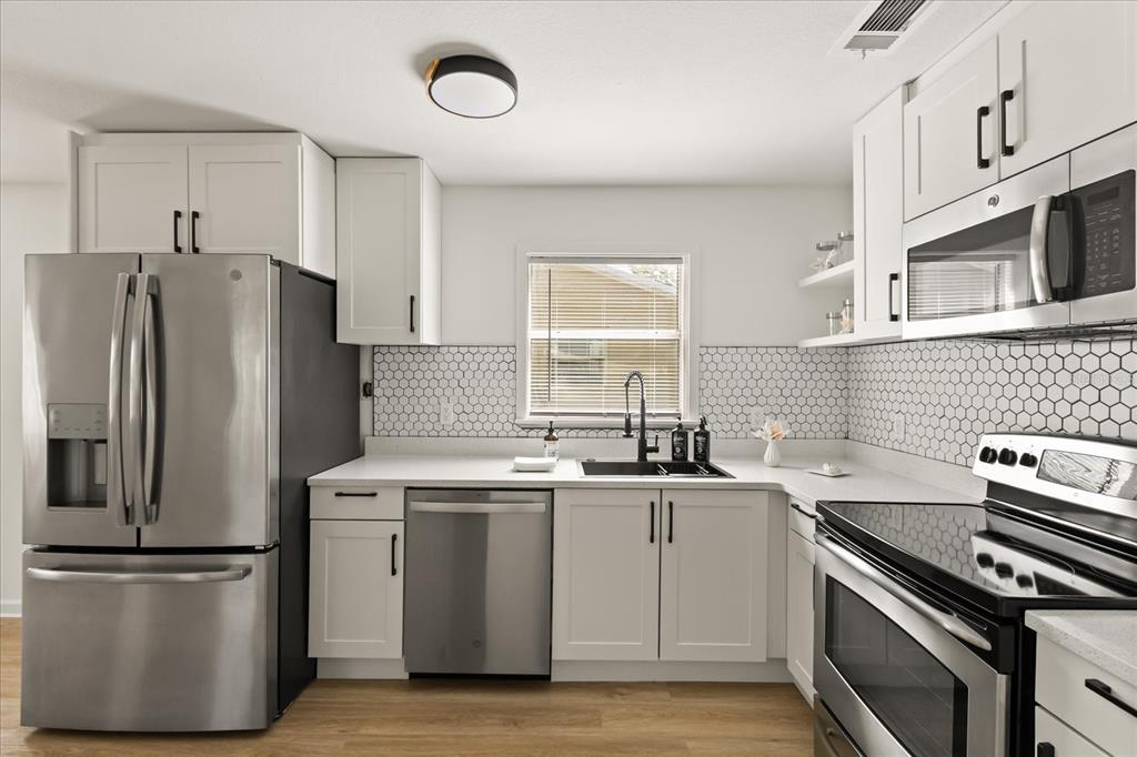 A kitchen with white cabinets, stainless steel appliances, a hexagon tile backsplash, and wood flooring — 2312 SW FORT KING STREET, OCALA, FL