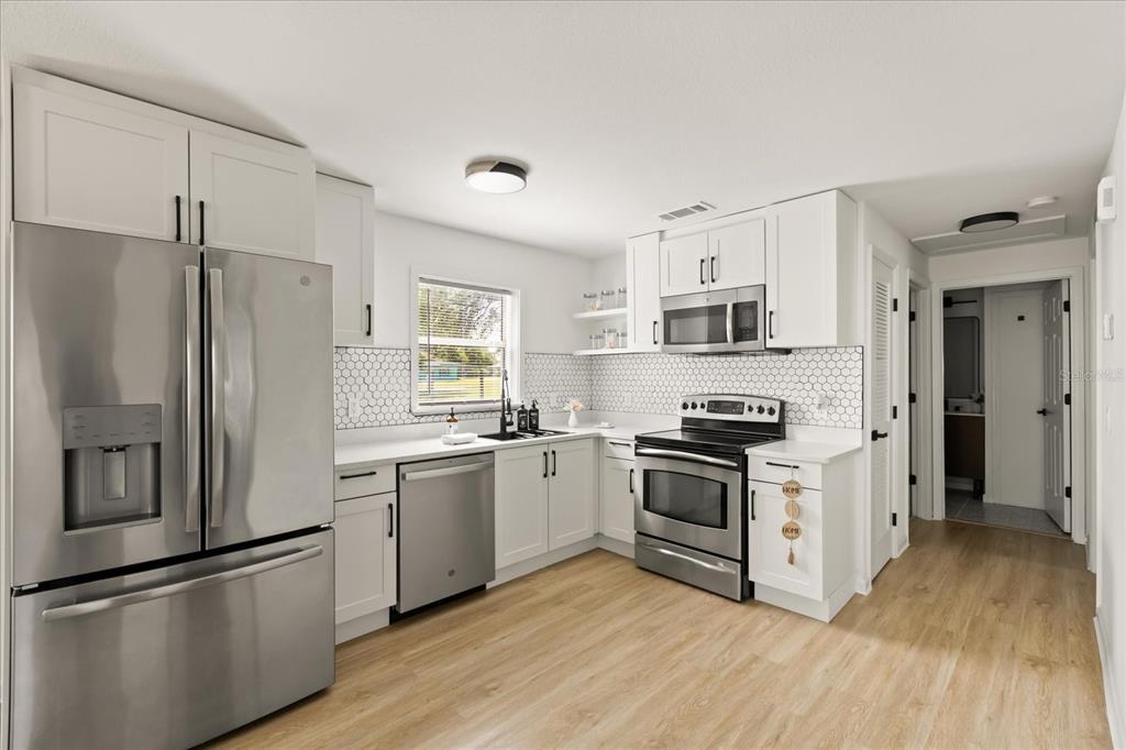 A modern kitchen features white cabinets, stainless steel appliances, a hexagon tile backsplash, and wood flooring — 2312 SW FORT KING STREET, OCALA, FL