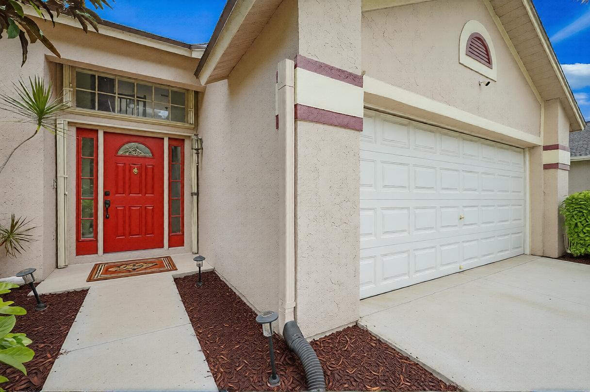 A red front door and a white garage door on a beige stucco house exterior — 3570 Woods Walk Boulevard, Lake Worth FL 33467, LAKE WORTH, FL
