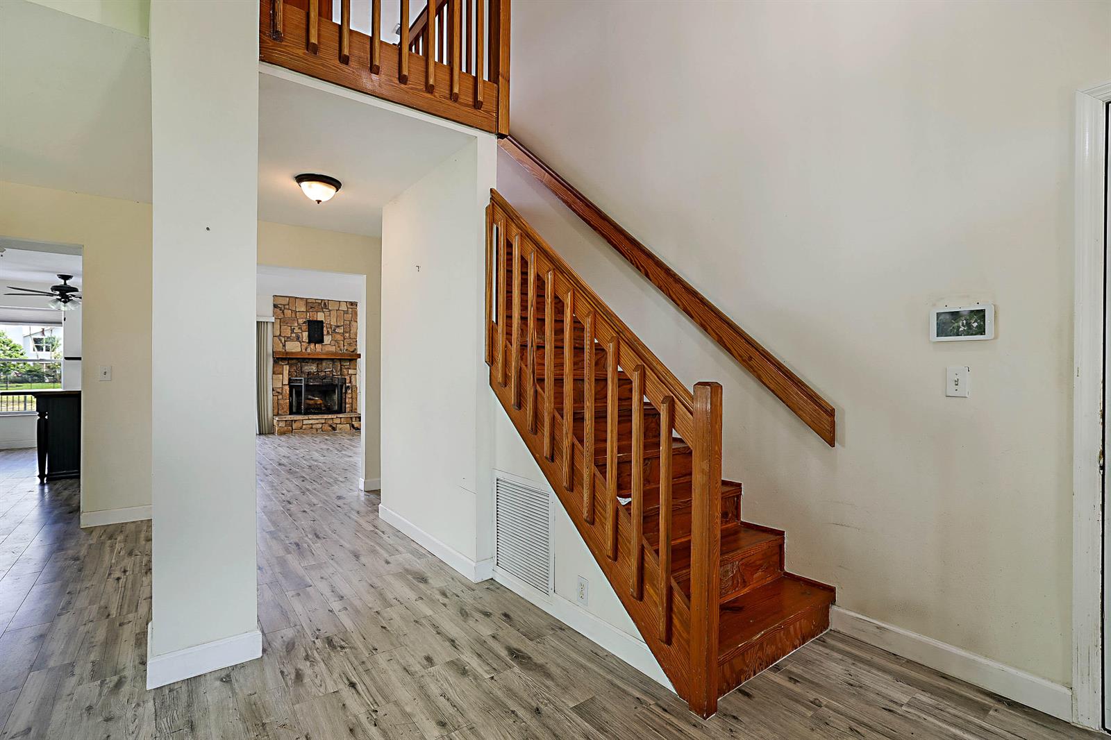 A wooden staircase with a railing stands in a foyer with light wood-look flooring — 3570 Woods Walk Boulevard, Lake Worth FL 33467, LAKE WORTH, FL