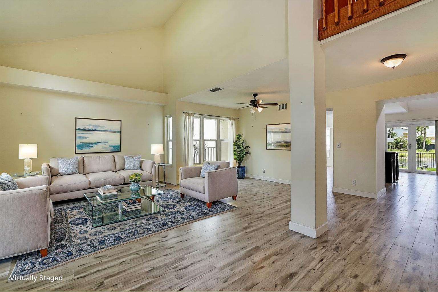A virtually staged living room features vaulted ceilings, light wood-look flooring, and a large rug — 3570 Woods Walk Boulevard, Lake Worth FL 33467, LAKE WORTH, FL