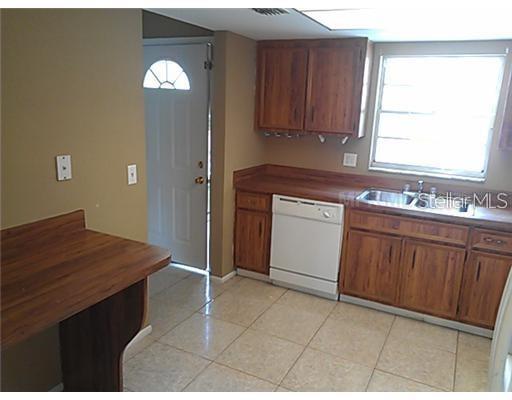 A kitchen features wood cabinets, a white dishwasher, a sink, and light-colored tile flooring — 7922 TOLER COURT, ORLANDO, FL