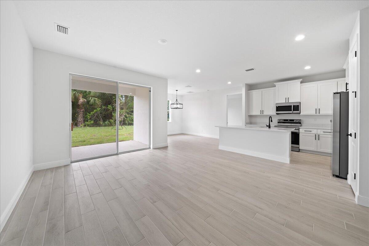A modern open-concept kitchen and living area with light wood-look tile floors and sliding doors — 5968 Birch Drive, Fort Pierce FL 34982, FORT PIERCE, FL